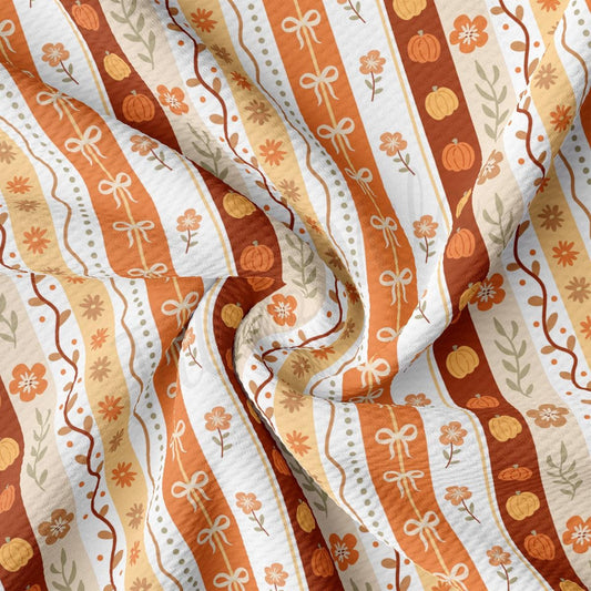 The image is a close-up view of a fabric with a repeating pattern of orange and white stripes, along with floral and pumpkin motifs.