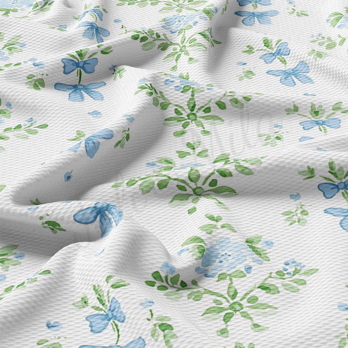a close-up view of a fabric with a floral pattern of blue flowers and green leaves. The fabric appears to be white, and the pattern is intricate and detailed.