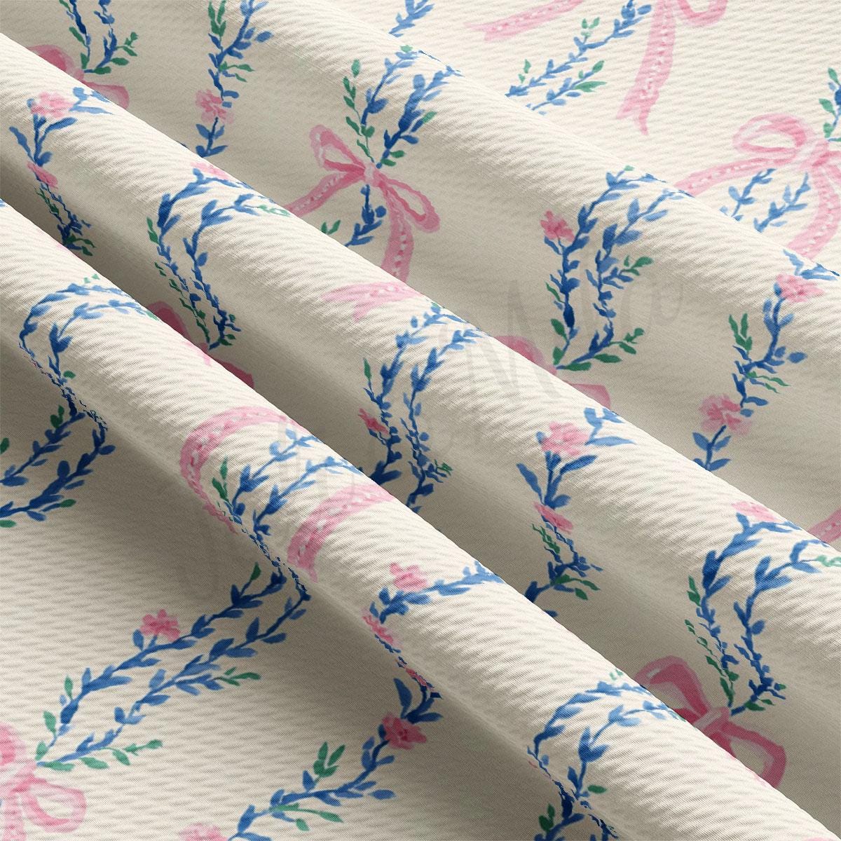 a close-up view of a fabric with a floral pattern in shades of pink and blue. The fabric appears to be folded or rolled, revealing the intricate design of the floral motifs.