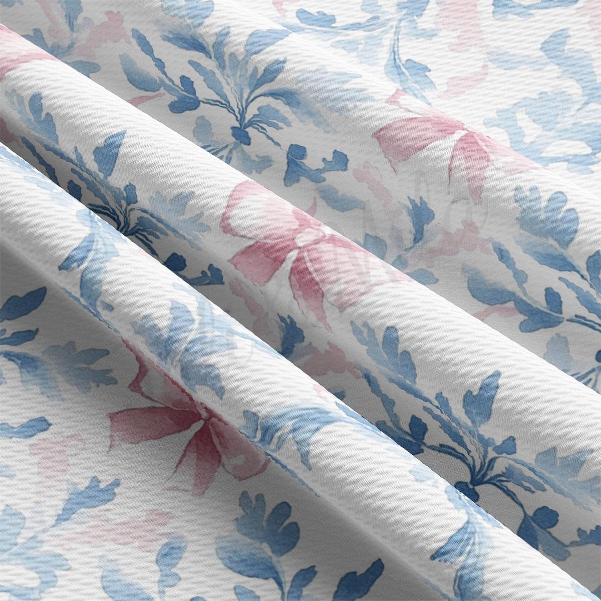 a close-up view of a fabric with a floral pattern in shades of blue and pink. The fabric appears to be made of a soft, textured material, possibly cotton or linen. The pattern consists of various floral designs, including leaves, flowers, and bows, which are spread across the fabric in a repeating pattern. The fabric is folded and crumpled, giving it a slightly wrinkled appearance.