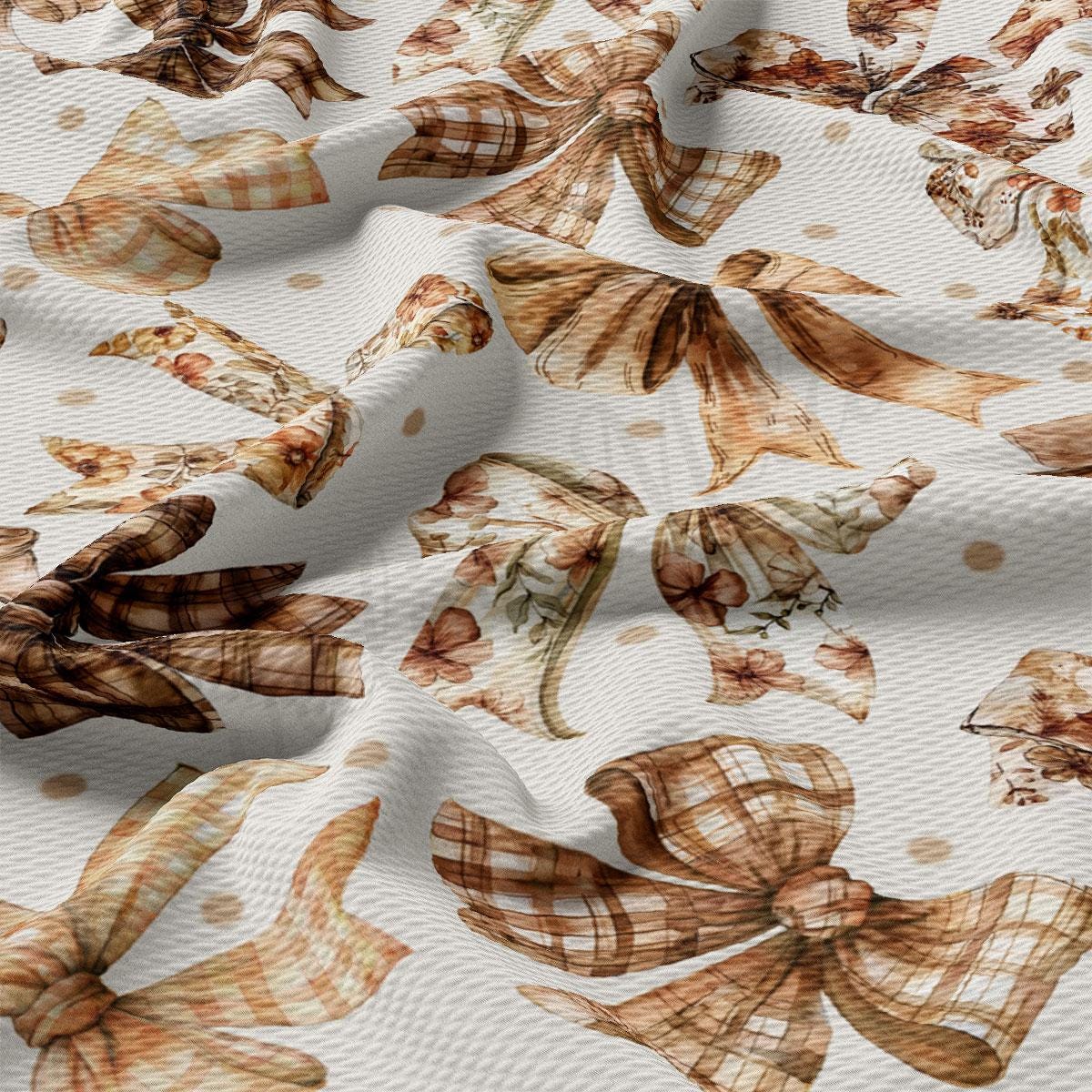 a close-up view of a fabric with a repeating pattern of brown and white bows and flowers. The bows appear to be made of a plaid or checkered pattern, and the flowers are depicted in a watercolor style. The fabric has a textured appearance, with the bows and flowers creating a visually interesting and intricate design.
