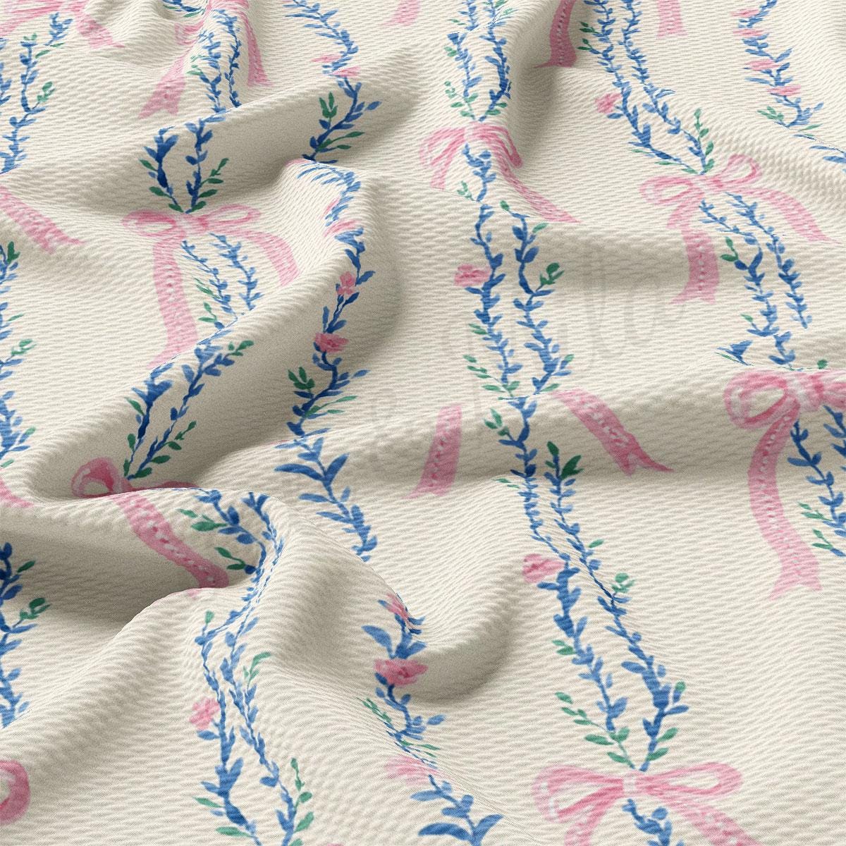 a close-up view of a fabric with a floral pattern, featuring pink and blue ribbons and leaves. The fabric appears to be crumpled, giving it a soft and delicate appearance.