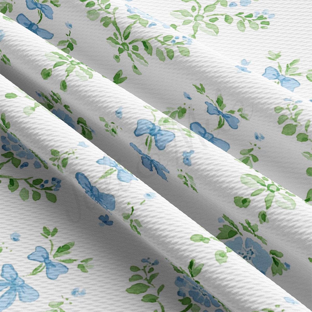 a close-up view of a fabric with a floral pattern in shades of blue and green. The fabric appears to be white, and the pattern consists of various blue flowers and green leaves. The fabric is folded and crumpled, giving it a textured appearance.