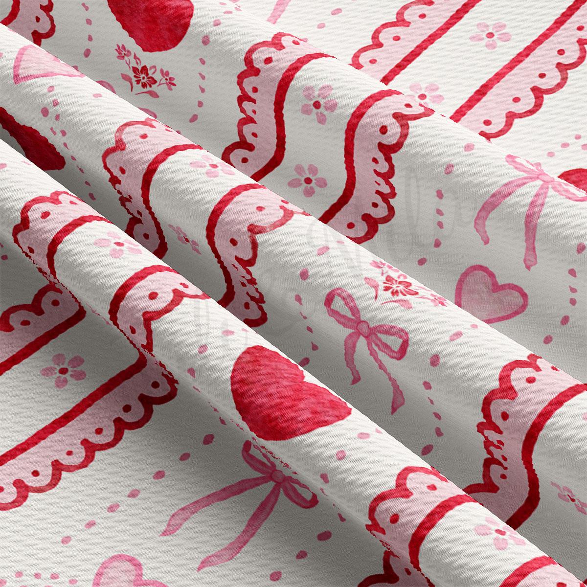 The image is a close-up view of a fabric with a repeating pattern of red hearts and pink bows. The fabric appears to be white, and the pattern is intricate and detailed.