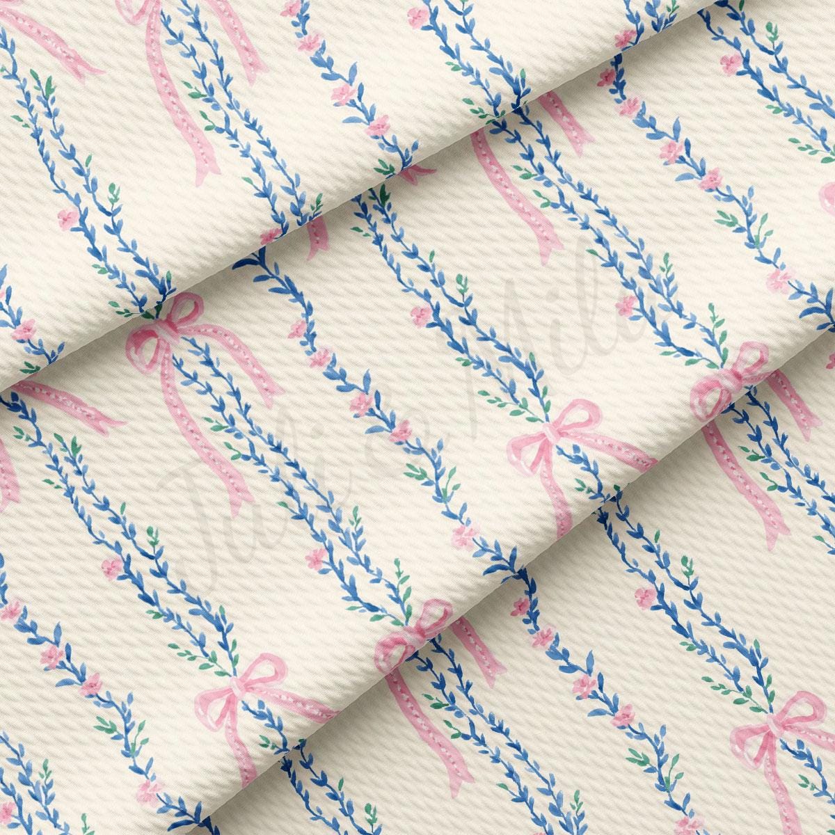 a close-up view of a fabric with a repeating pattern of pink bows and blue leaves. The pattern is arranged in a diagonal line across the fabric, creating a visually appealing and intricate design.