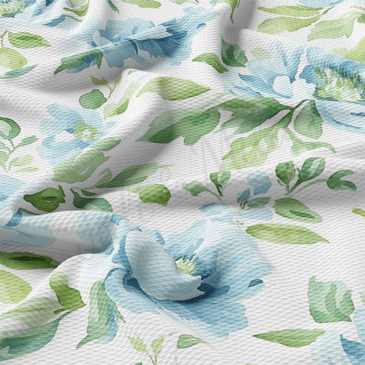 a close-up view of a fabric with a floral pattern, including blue and green flowers and leaves. The fabric appears to be white, and the pattern is intricate and detailed.