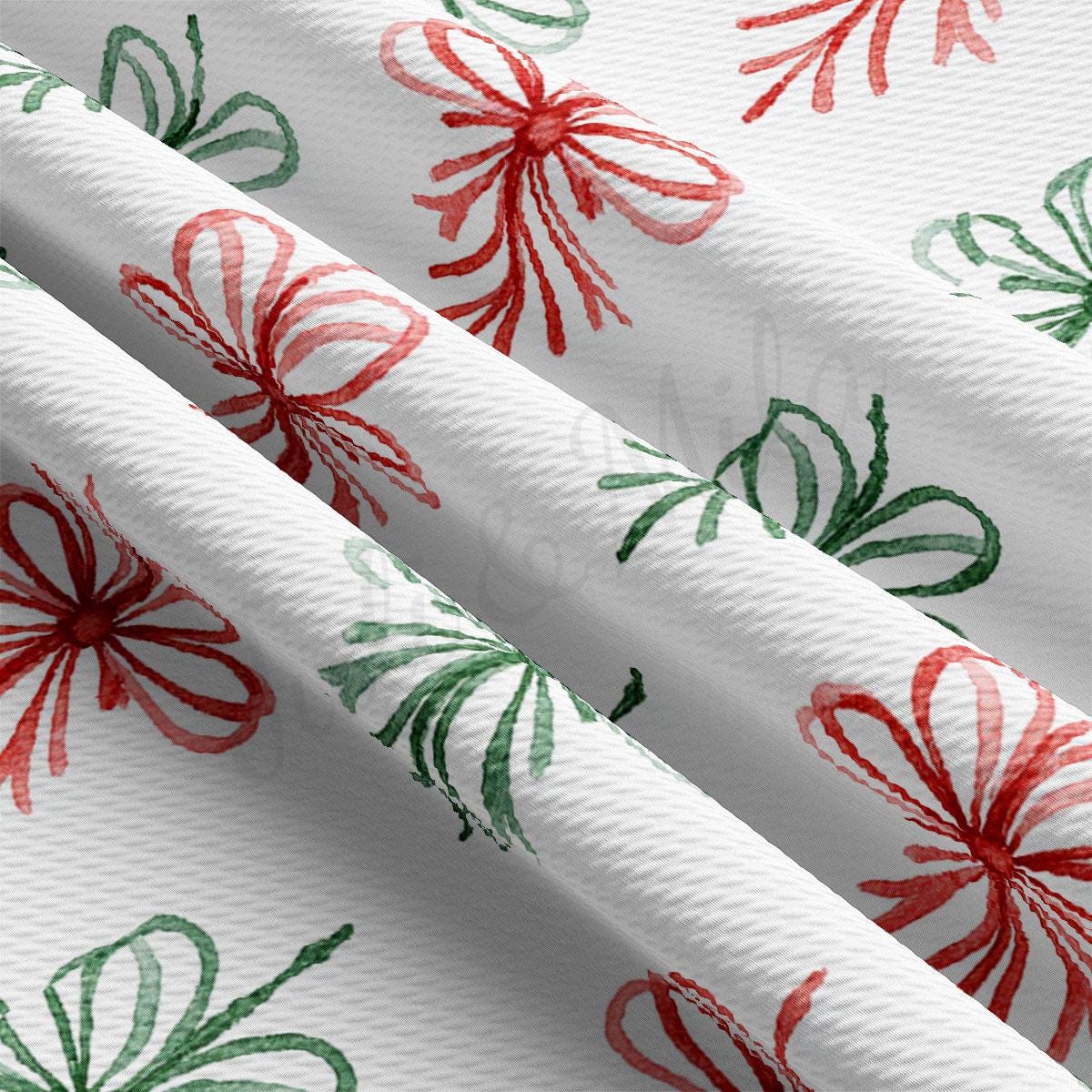 a close-up view of a fabric with a repeating pattern of red and green bows on a white background.