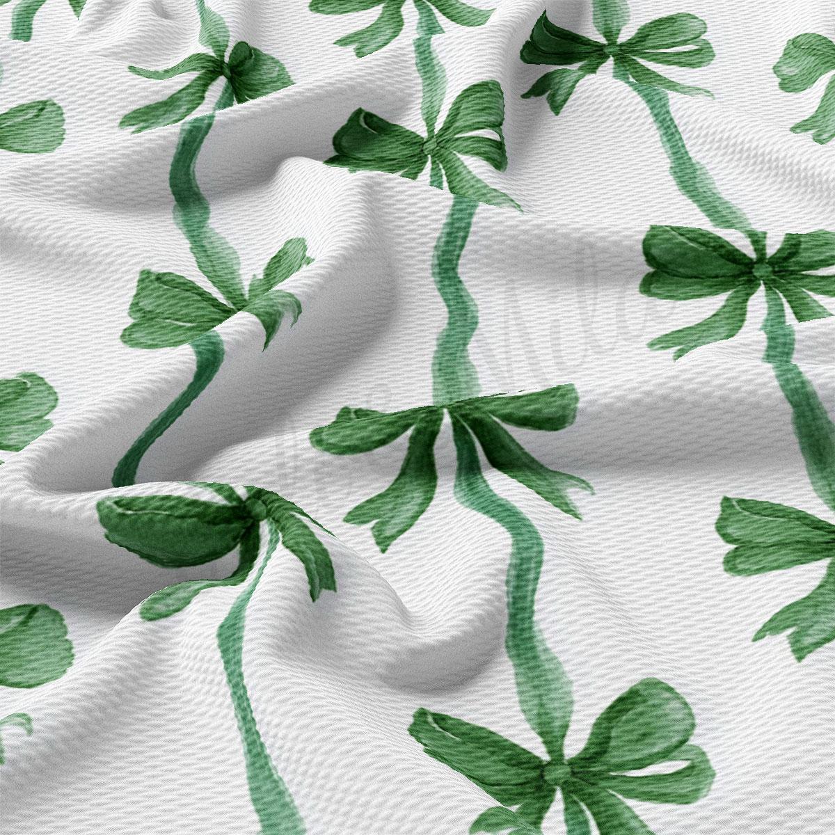 a close-up view of a white fabric with a repeating pattern of green bows and leaves.