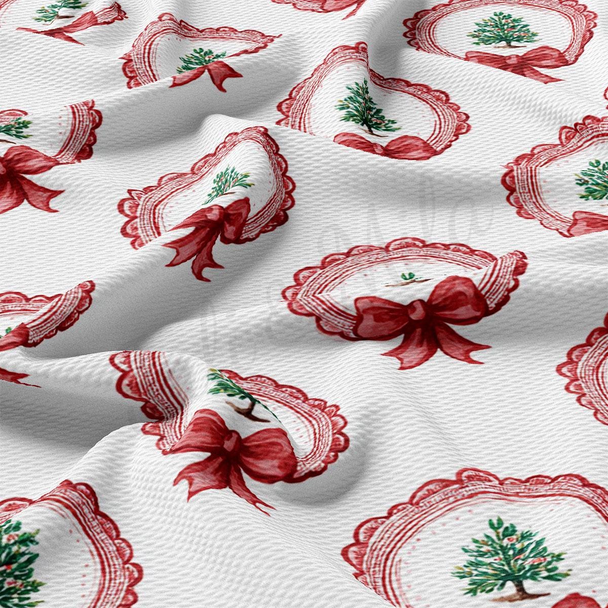 a close-up view of a fabric with a repeating pattern of red bows and Christmas trees. The bows are arranged in a circular pattern, and the Christmas trees are depicted in a stylized manner. The fabric appears to be made of a soft, white material, and the overall design has a festive and holiday-themed appearance.